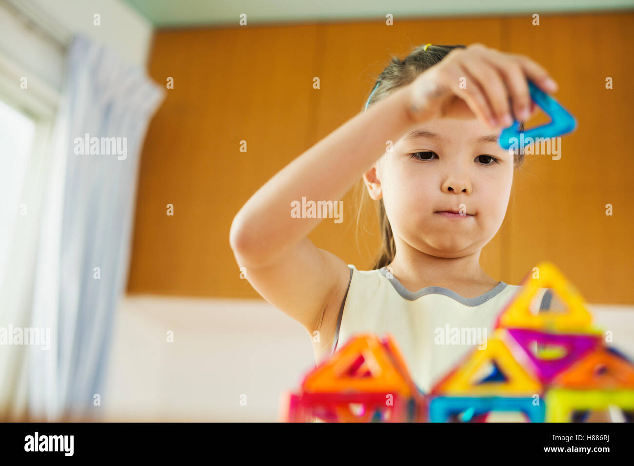 A girl playing, building a structure with colourful geometric shapes. Stock Photo