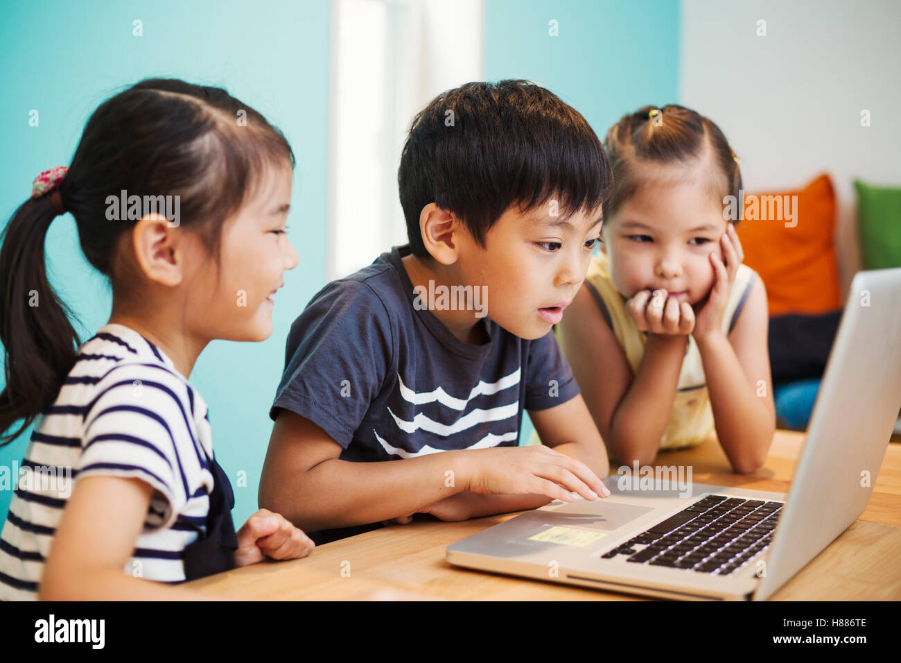 Three children using a laptop, two girls and a boy. Stock Photo