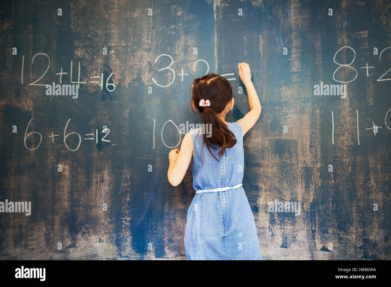 A group of children in school. A girl writing in chalk on a chalkboard. Stock Photo