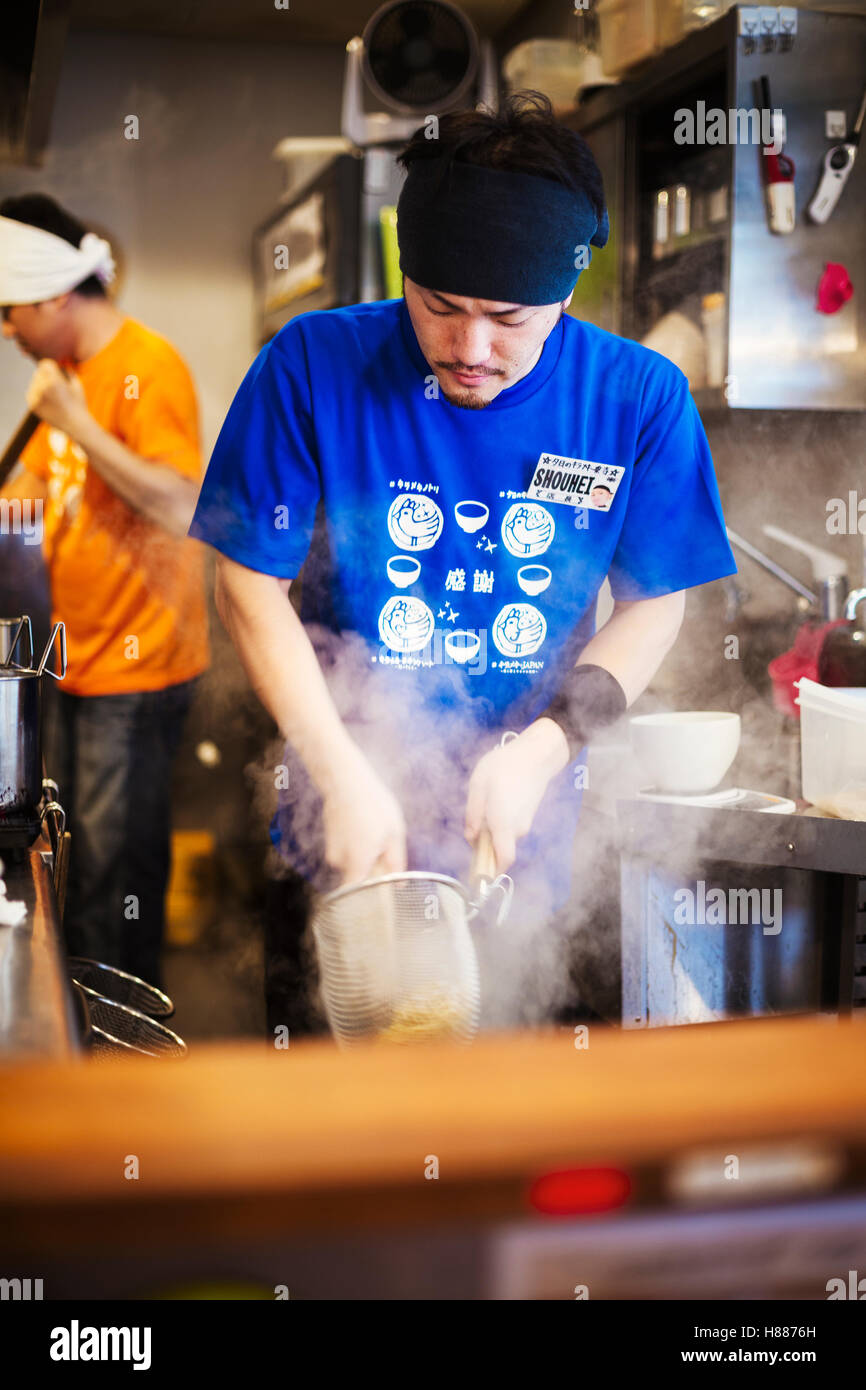 A ramen noodle shop kitchen. A chef preparing bowls of ramen noodles in