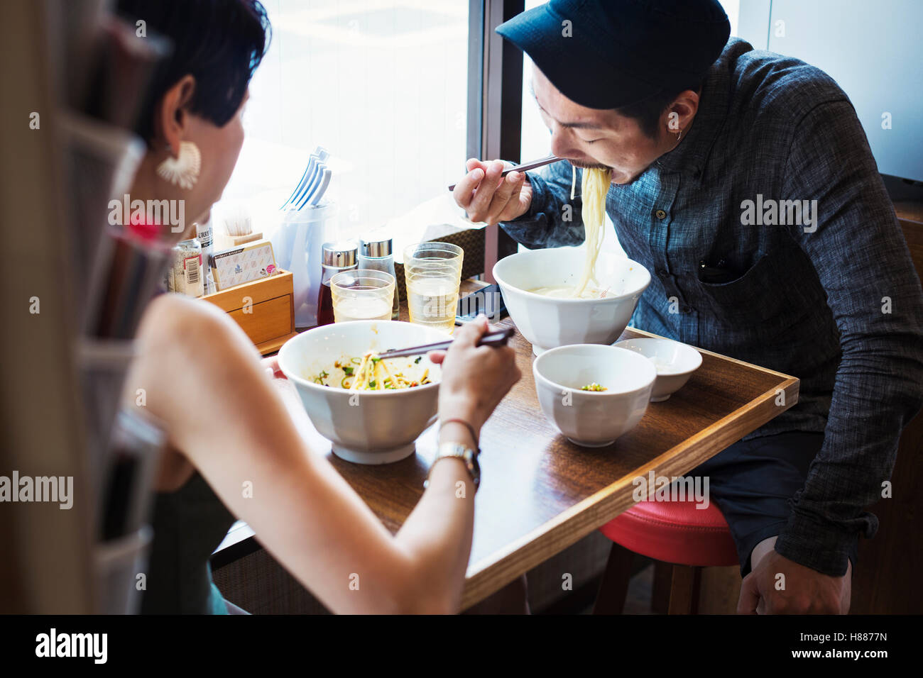 A ramen noodle cafe in a city.  A man and woman seated eating noodles from large white bowls. Stock Photo