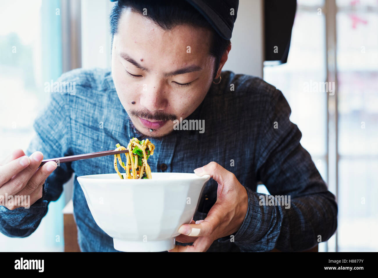 A ramen noodle cafe in a city.  A man seated eating ramen noodles from a large broth bowl. Stock Photo