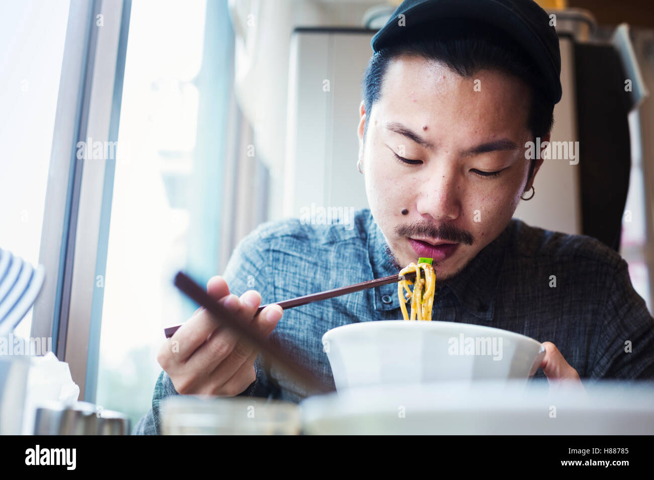 A ramen noodle cafe in a city.  A man sitting eating ramen noodle soup dish. Stock Photo