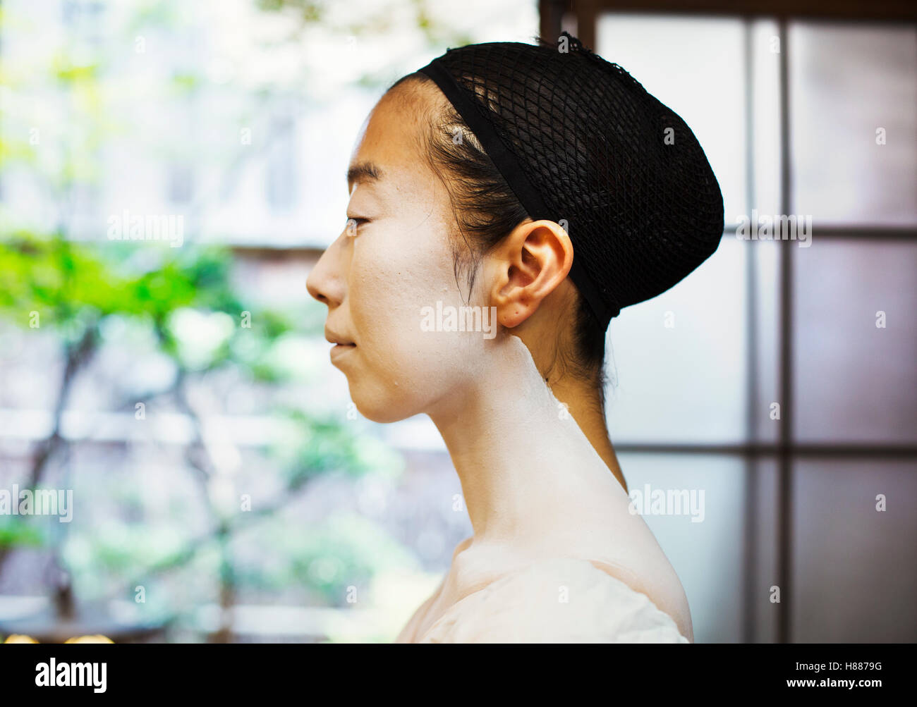 A modern geisha or maiko woman in traditional fashion, with white face makeup. Profile. Stock Photo