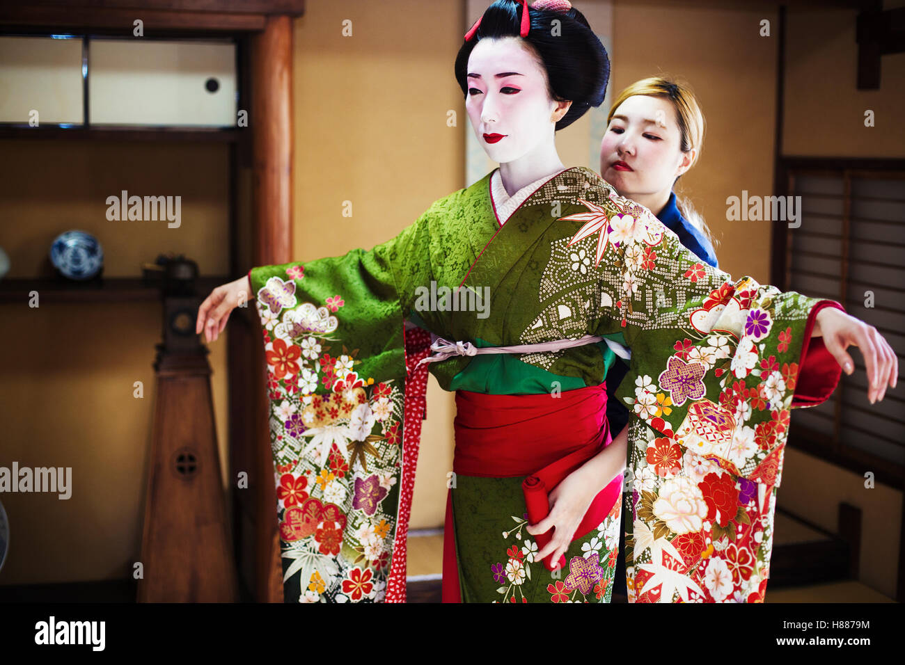 A woman being dressed in geisha style, wearing a kimono and obi, with an  elaborate hairstyle and floral hair clips Stock Photo - Alamy