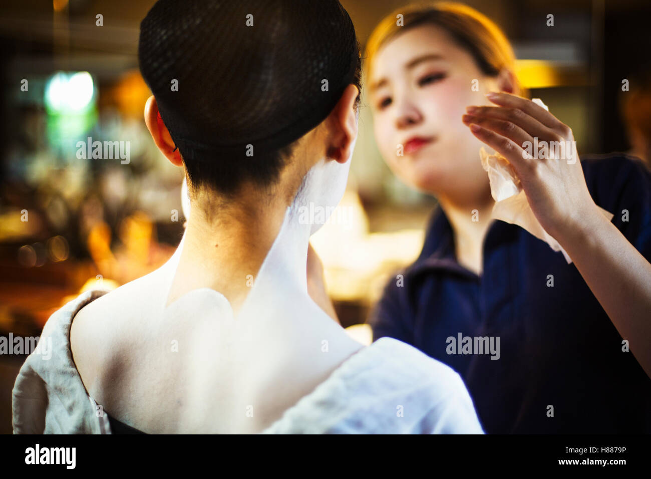 A modern geisha or maiko woman being made up in traditional fashion, with white makeup on her neck and shoulders. Stock Photo