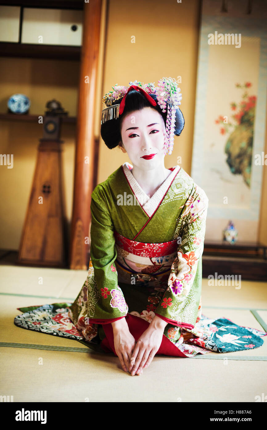 A woman dressed in the traditional geisha style, wearing a kimono and obi, with an elaborate hairstyle Kneeling on the floor. Stock Photo