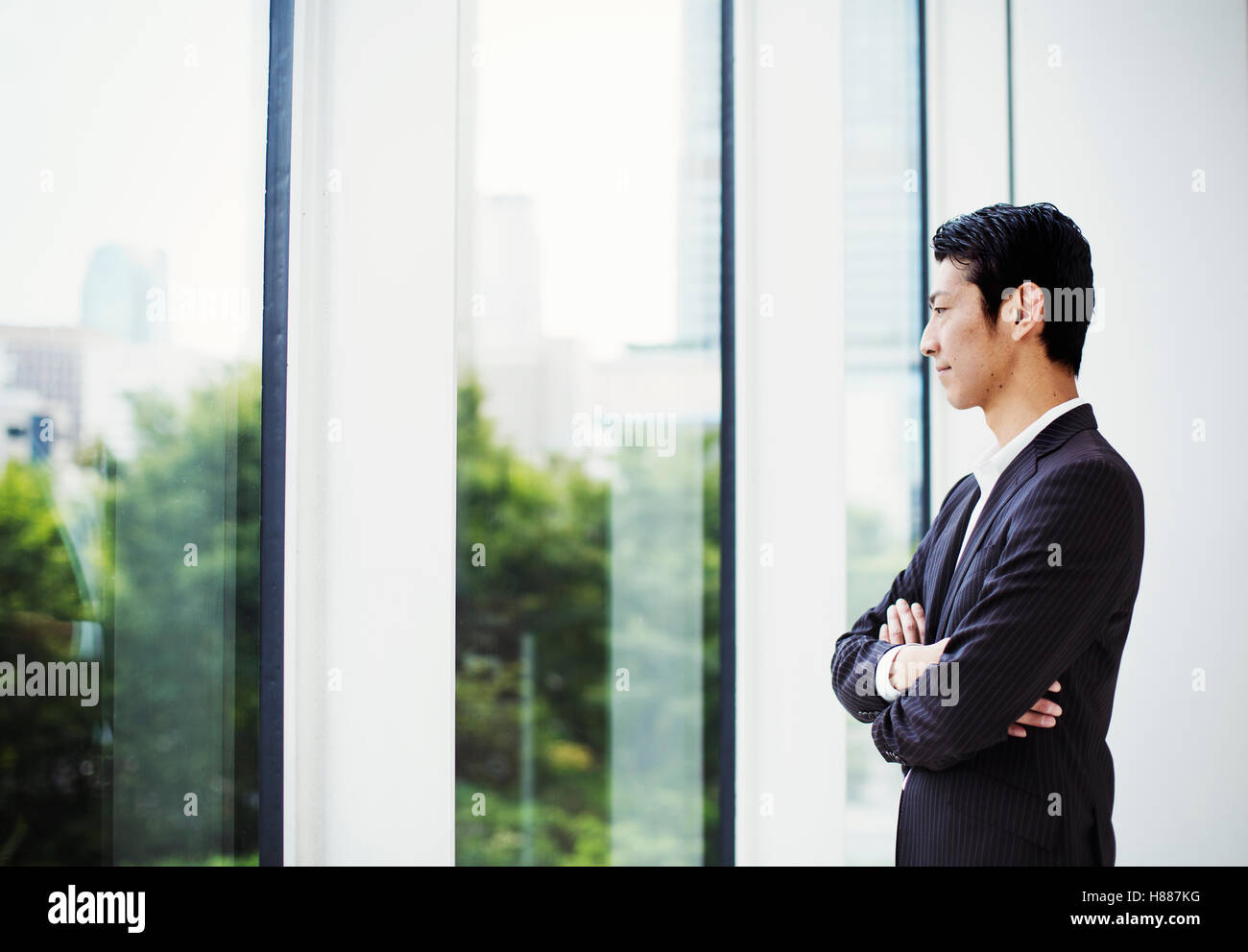 A businessman in the office, by a large window, looking out. Stock Photo