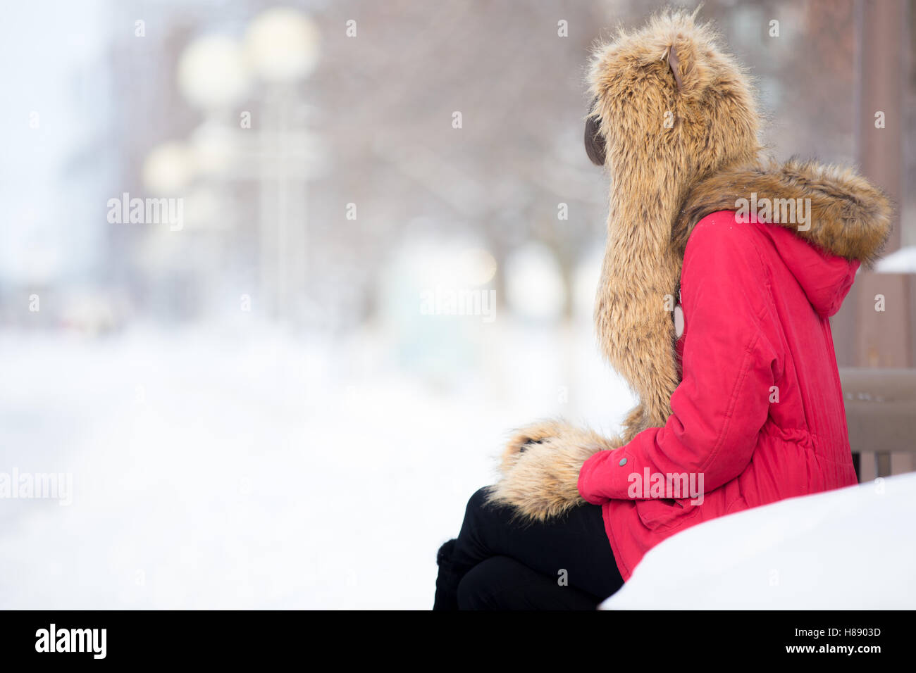 Lonely woman sitting on the bench outdoors in wintertime Stock Photo