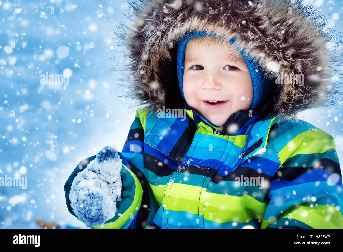 Boy in knitted hat, gloves and scarf outdoors at snowfall Stock Photo
