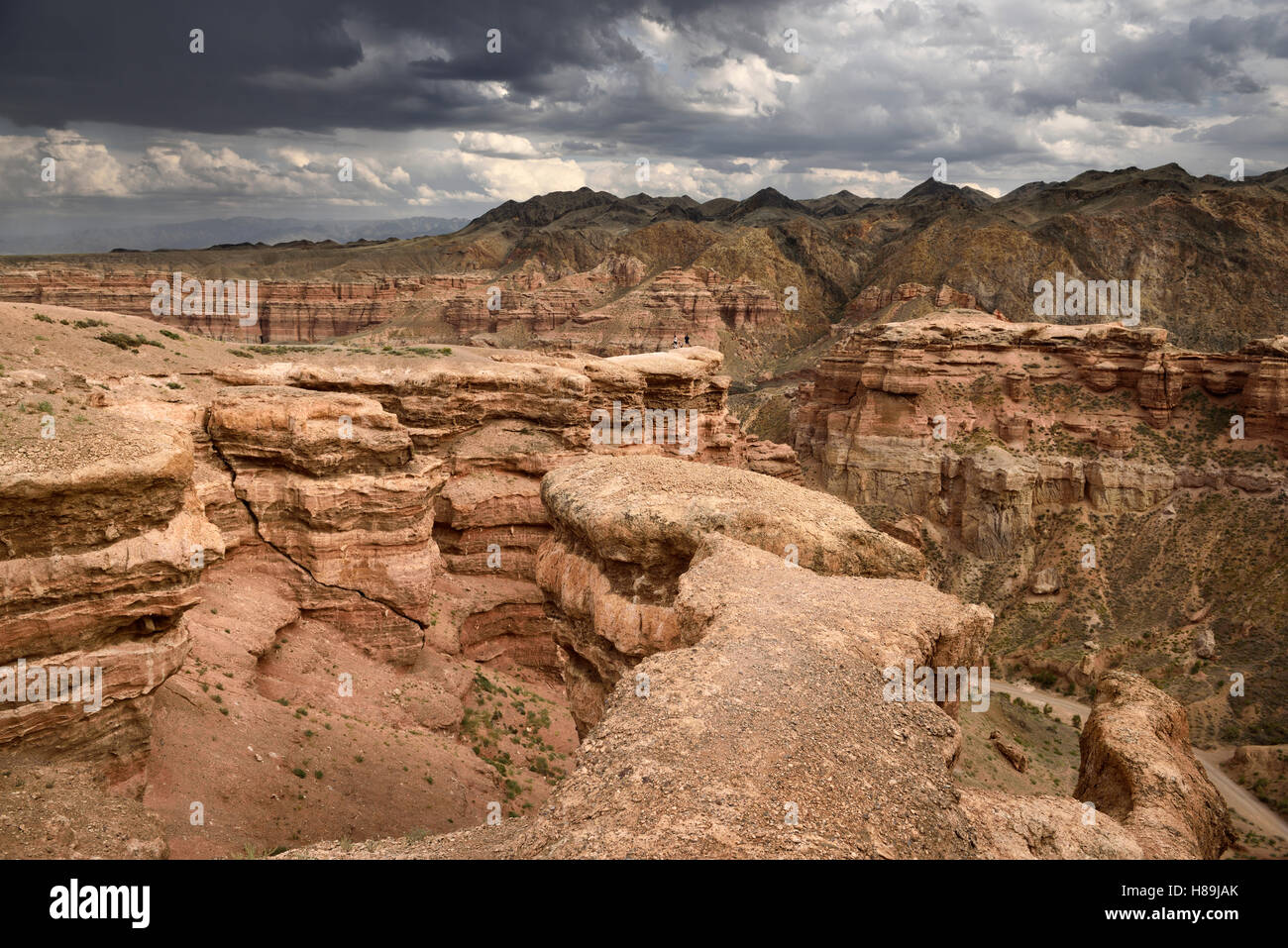 Tourists on cliff top at Charyn Canyon Park with clouds and Tien Shen mountains Kazakhstan Stock Photo