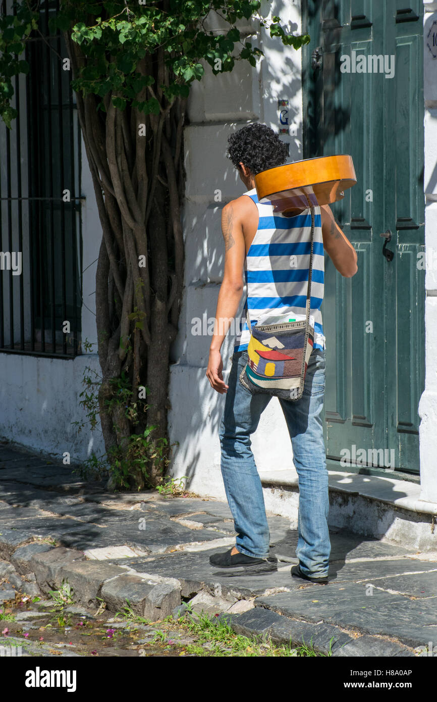 Man walking with his guitar on the shoulder along a street in Colonia del Sacramento, Uruguay Stock Photo