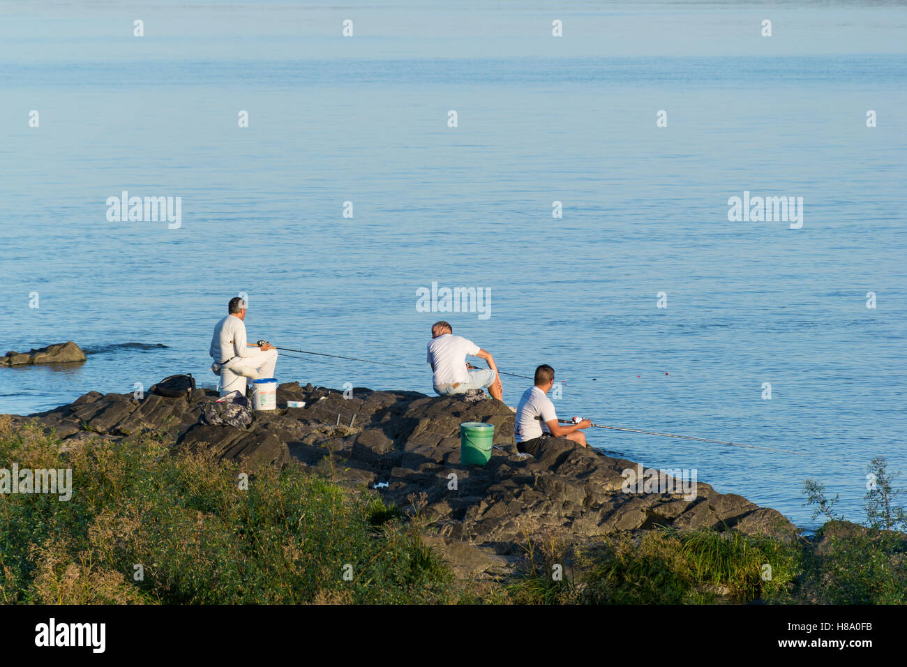 Three fishermen over a rocky shore fishing in the Río de la Plata at the twilight Stock Photo