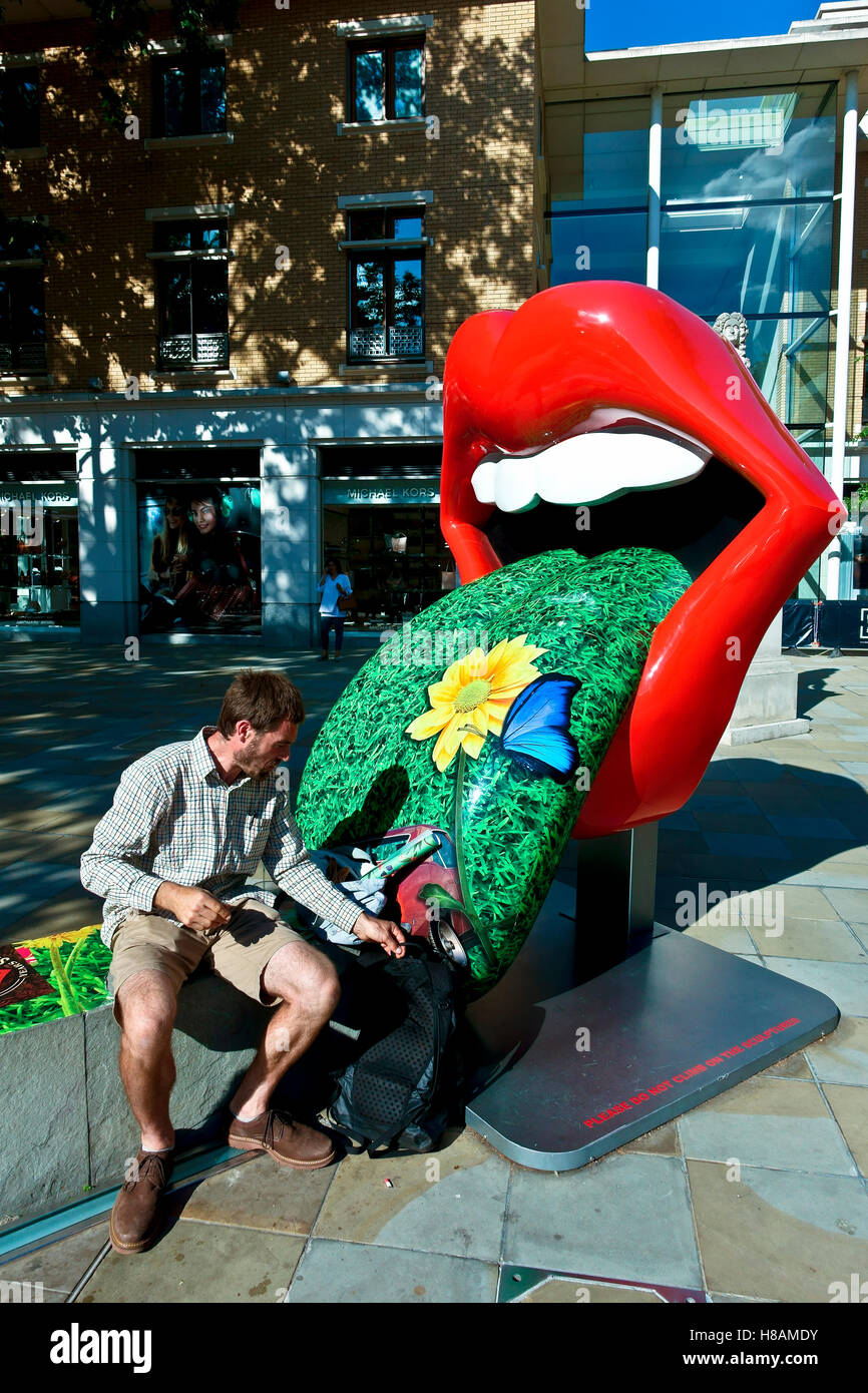 Man sitting on a bench, lip display for The Rolling Stones Exhibitionism retrospective show at the Saatchi Gallery, King's Road, Chelsea, Lundon, UK Stock Photo