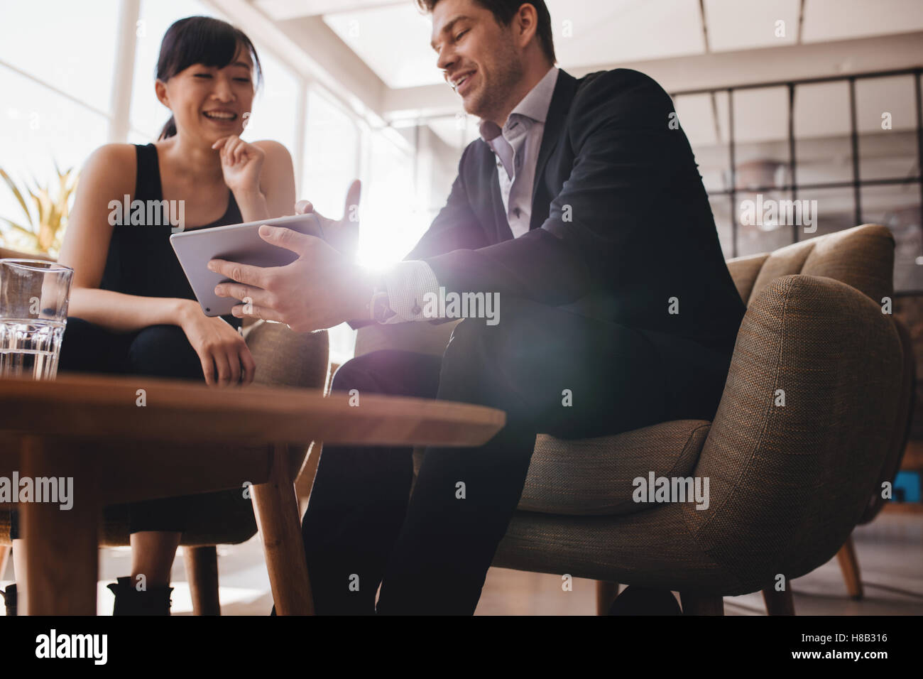 Two business people sitting at lobby and discussing project on digital tablet. Young businesswoman and businessman looking at ta Stock Photo