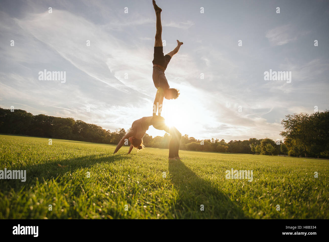Outdoor shot of young man and woman doing yoga in pair. Couple doing acrobatic yoga exercise at park. Stock Photo
