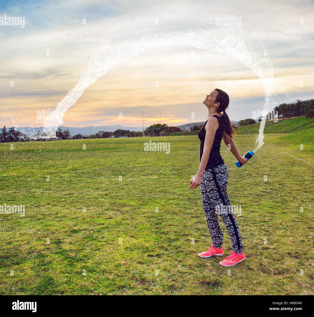 Woman having fun throwing water after outdoors workout at sunset Stock