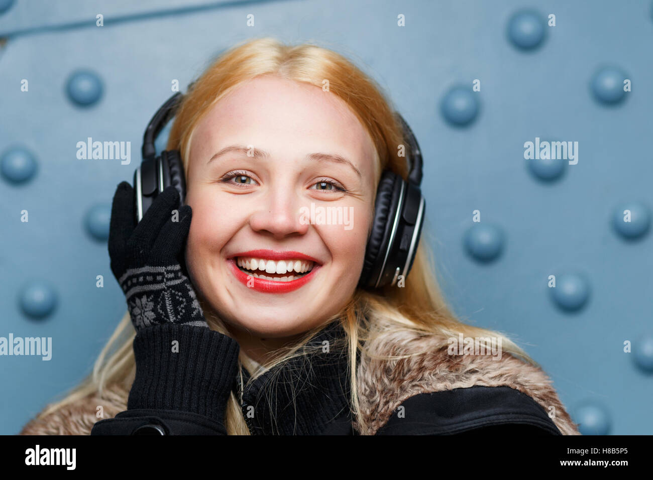 Laughing ginger girl with headphones closeup at blue wall Stock Photo