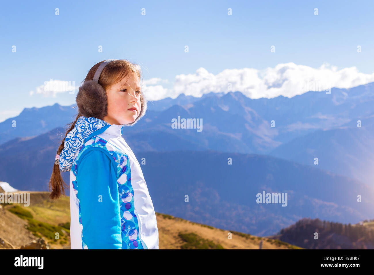 Girl with a pigtail, dressed in sports jacket and warm fluffy headphones, admires of autumn mountain landscape, Sochi, Russia Stock Photo