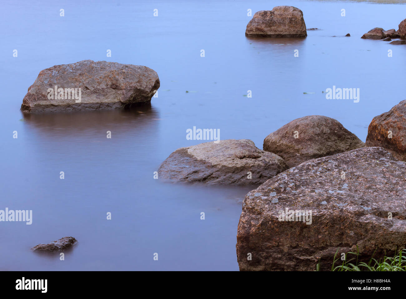 Stones on beach and huge rocks in calm water of Gulf of Vyborg. Evening calm in sea Bay, Leningrad, Saint-Petersburg, Russia Stock Photo