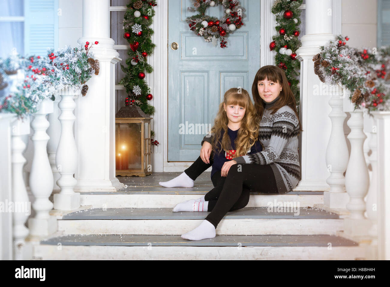 Mom and daughter in cozy home, decorated entrance to house with bright colours. Family waiting for New year. Family Christmas Stock Photo
