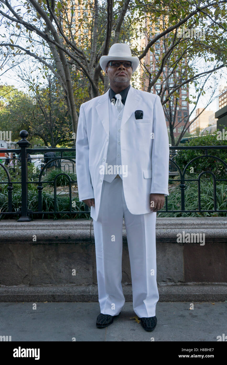 A stylish man in a white suit, tie & hat wearing a black shirt. In Union Square Park in New York City. Stock Photo