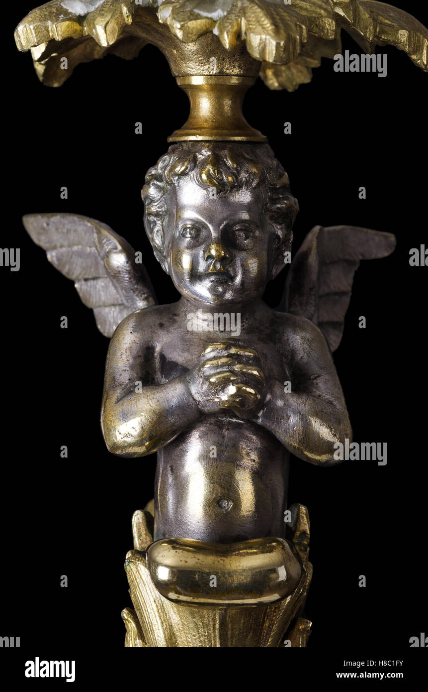 Praying brass angel on black background. A winged putto made of brass, covered with silver, as part of a candelabra. Stock Photo