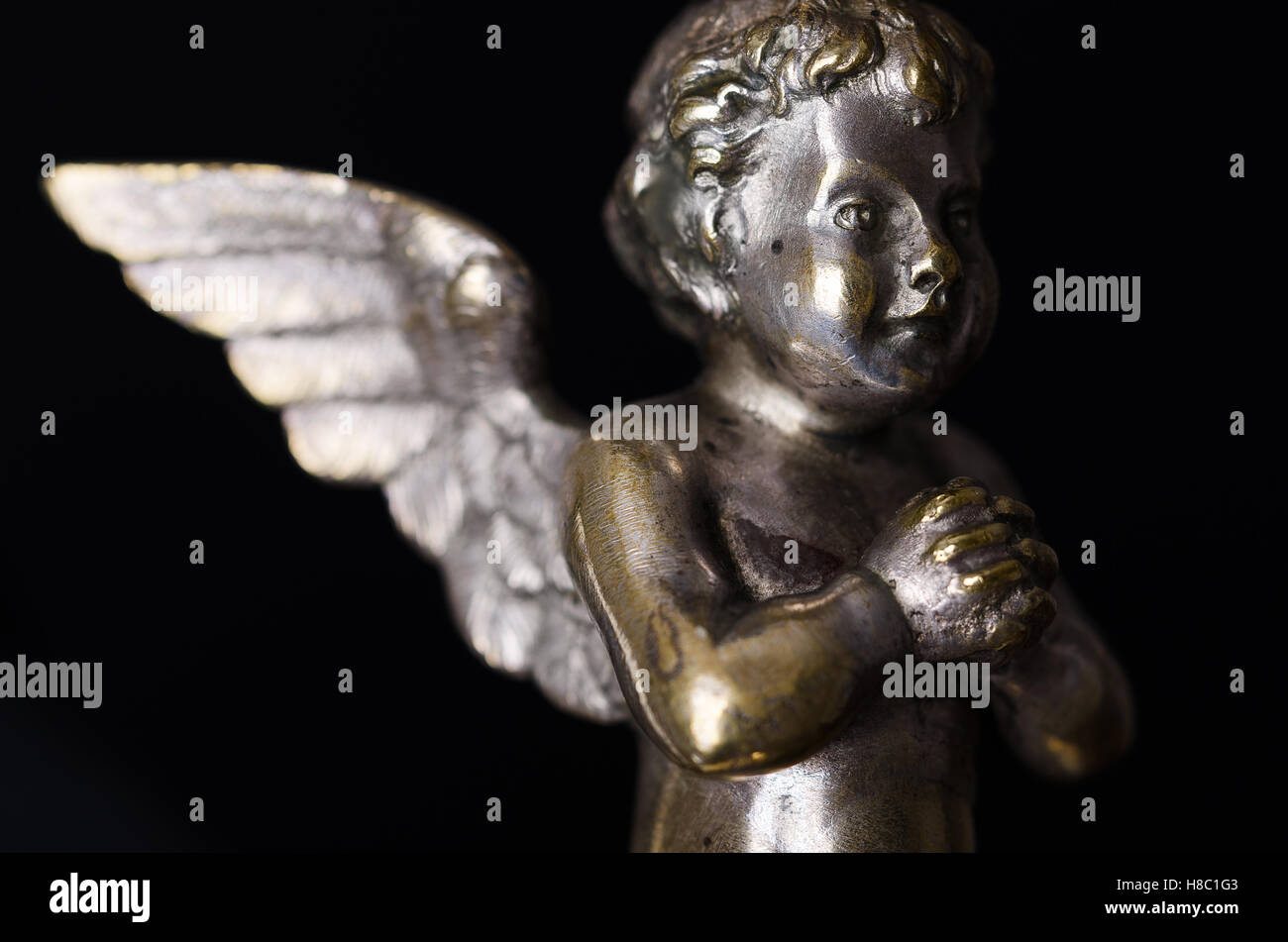 Praying brass angel side view over black. A winged putto made of brass, covered with silver, as part of a candelabra. Stock Photo
