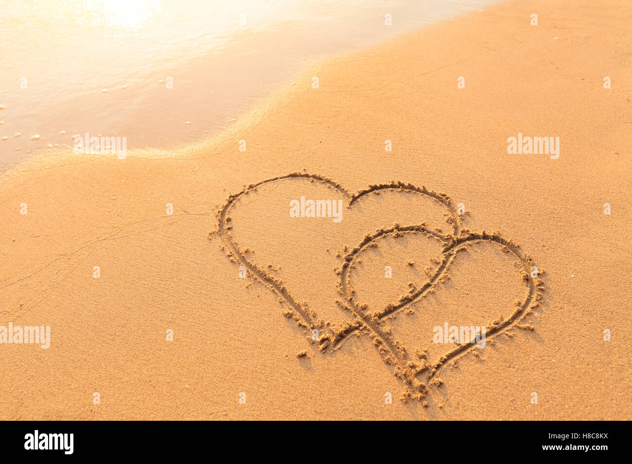 Shape of two hearts drawn in the sand of a tropical beach - symbol of love, honeymoon travel Stock Photo