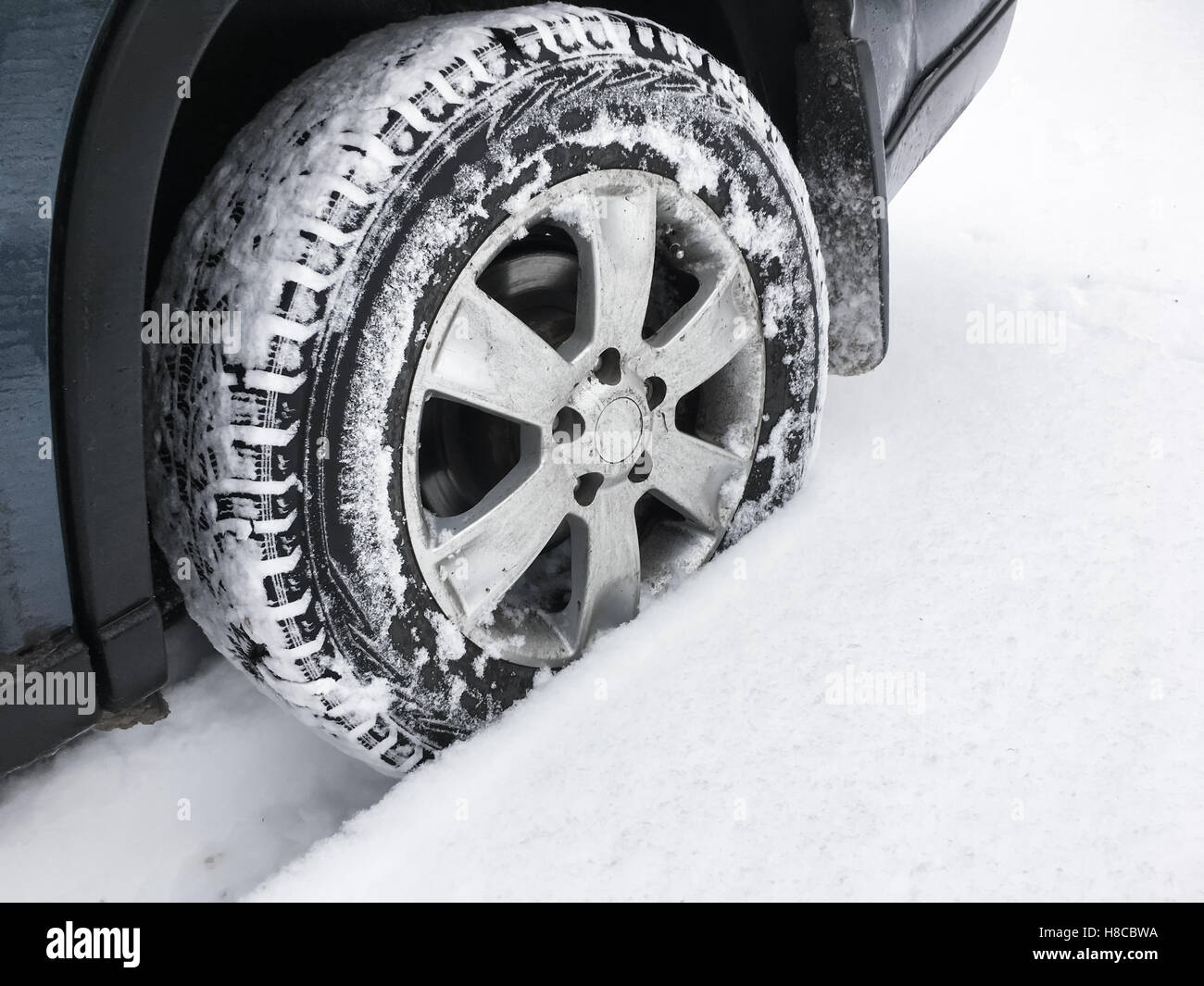 Modern car wheel with studded tire stands on winter road with deep snow, closeup photo with