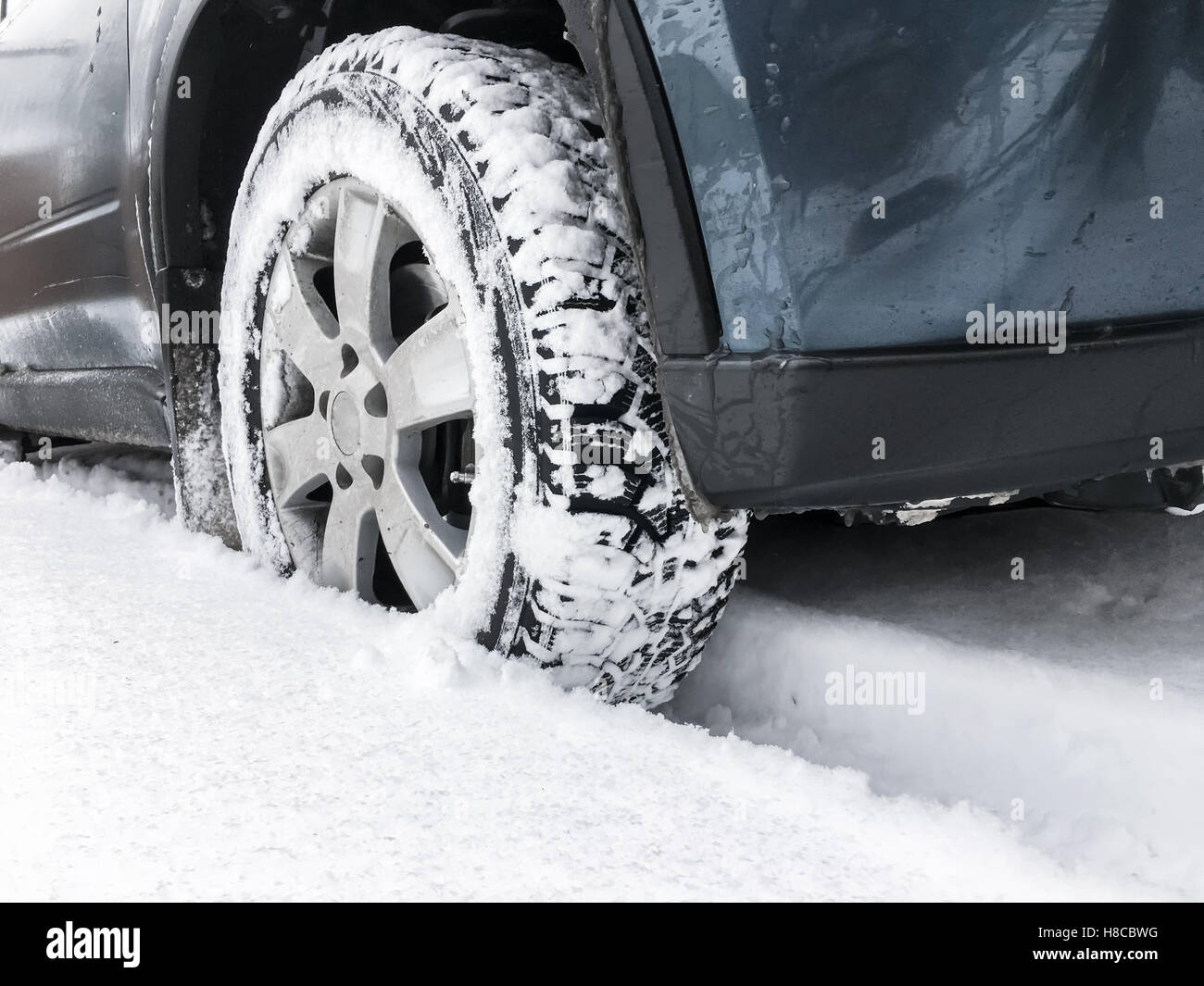 Modern blue car fragment, wheel with studded tire standing on winter