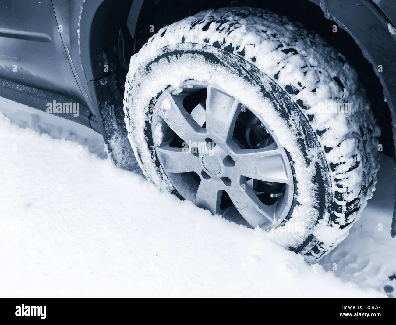 Car wheel with studded tire standing on winter road with deep snow