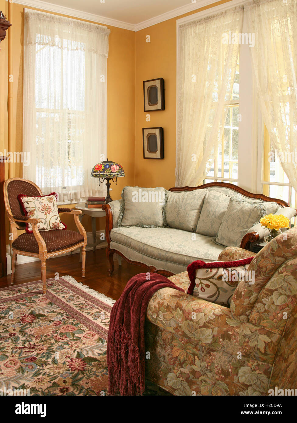 Yellow sitting room with upholstered sofa and floral patterned rug.. Stock Photo
