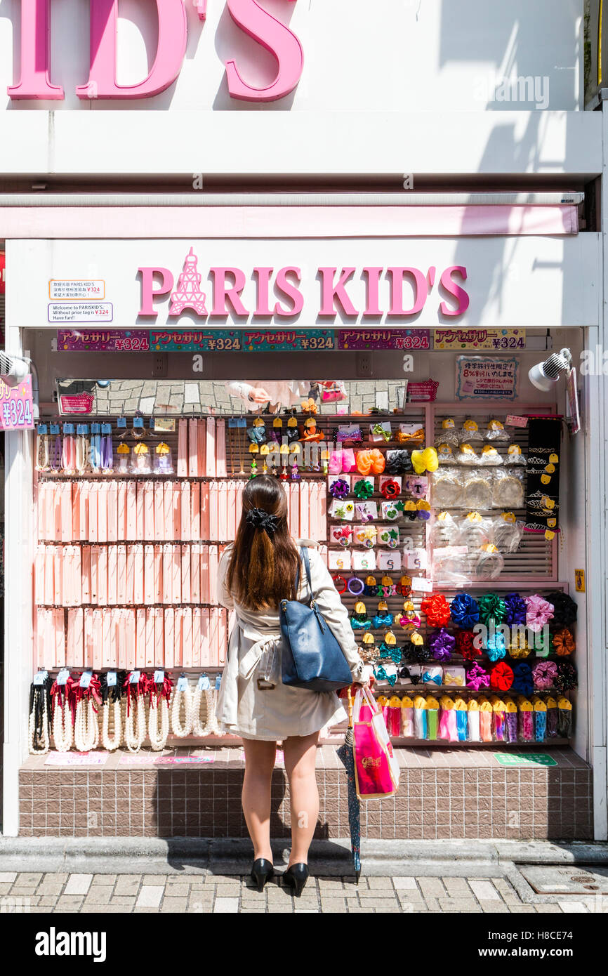 Japan, Tokyo, Harajuku, Takeshita-dori. Paris Kids women's fashion accessory store. Entrance. Young woman standing looking at display window. Stock Photo
