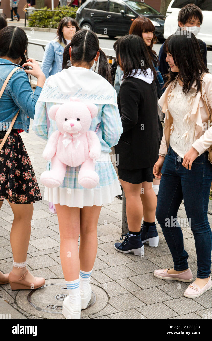 Japan, Tokyo, Harajuku. Back view of Lolita style fashion kawaii Japanese girl standing talking to friends. On back, pink teddy-bear rucksack. Stock Photo