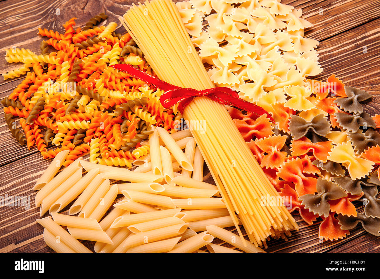 Spaghetti tied with a red ribbon, a number of different types of pasta, lying around on vintage wooden background Stock Photo