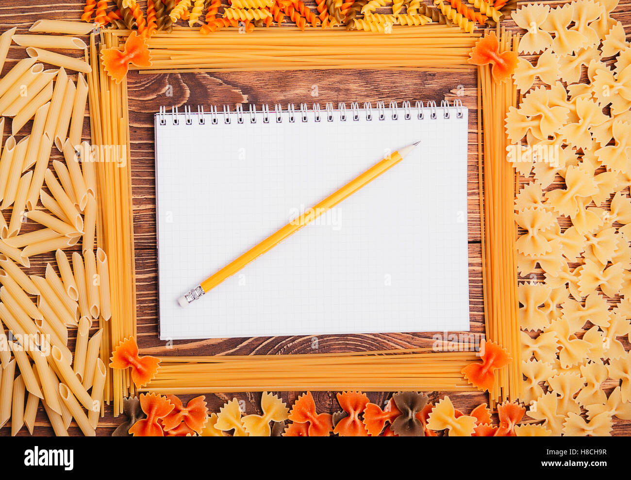 Pencil lying on a book of recipes frame of pasta on a wooden retro background Stock Photo