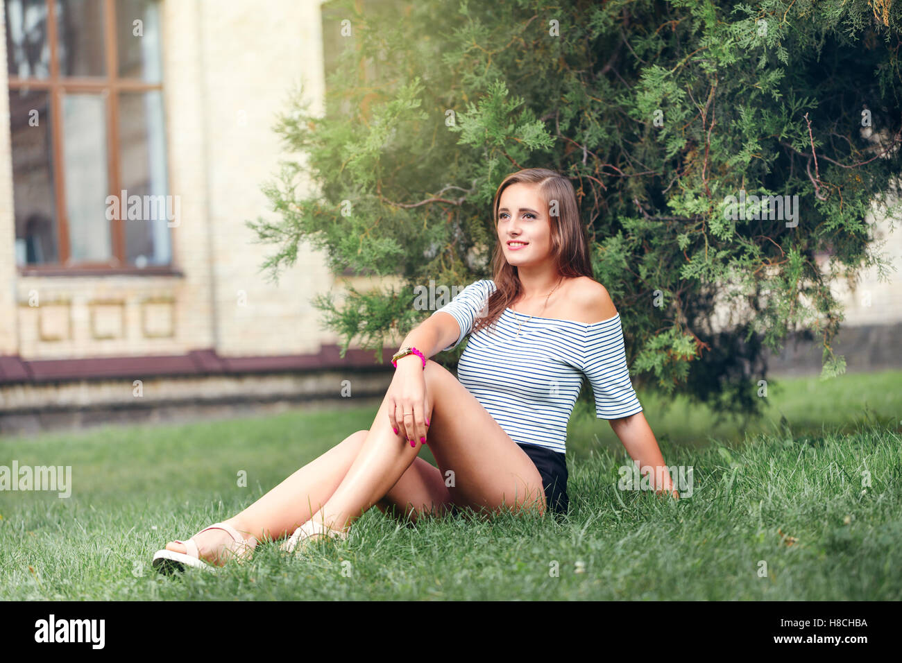 young beautiful happy woman sitting on the grass in the park Stock Photo