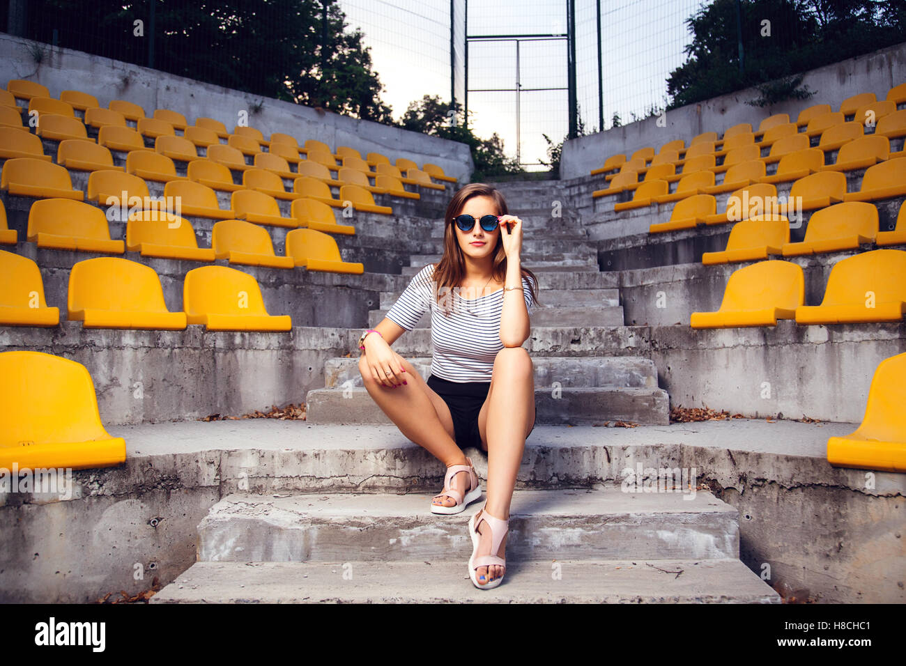 fashionable woman with round glasses sitting on the steps of the stadium Stock Photo