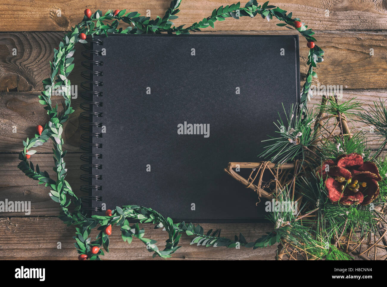 Image of black notebook mockup scene, with natural wood planks and christmas decorations. Stock Photo