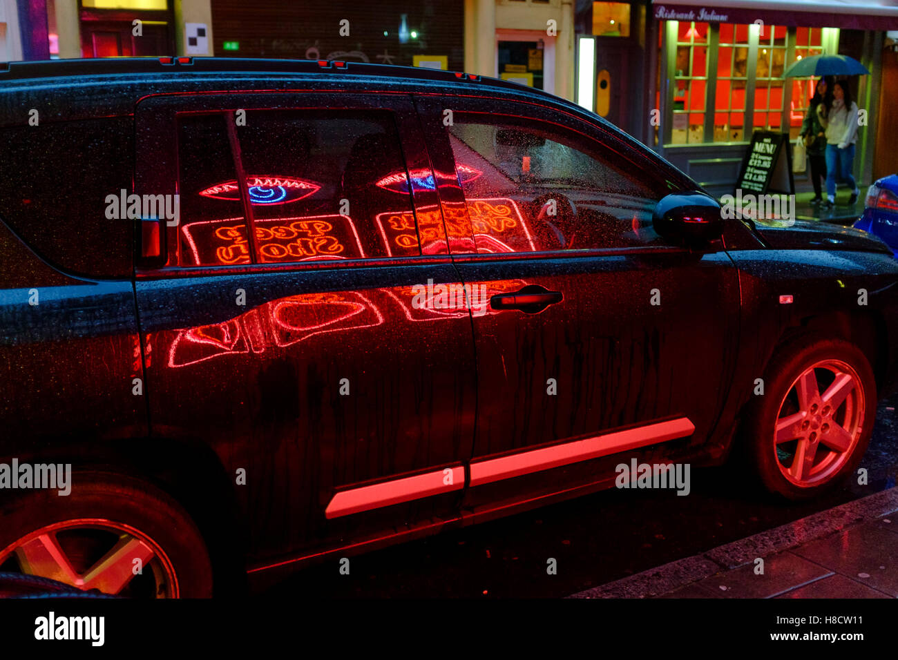 Neon sign of adult entertainment venue, reflected in parked vehicle Soho, London, UK Stock Photo