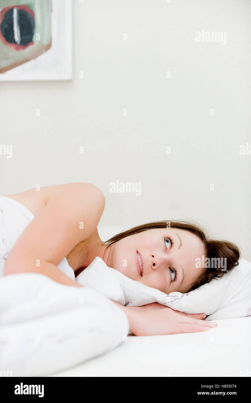 Young woman lying in bed, pensively Stock Photo