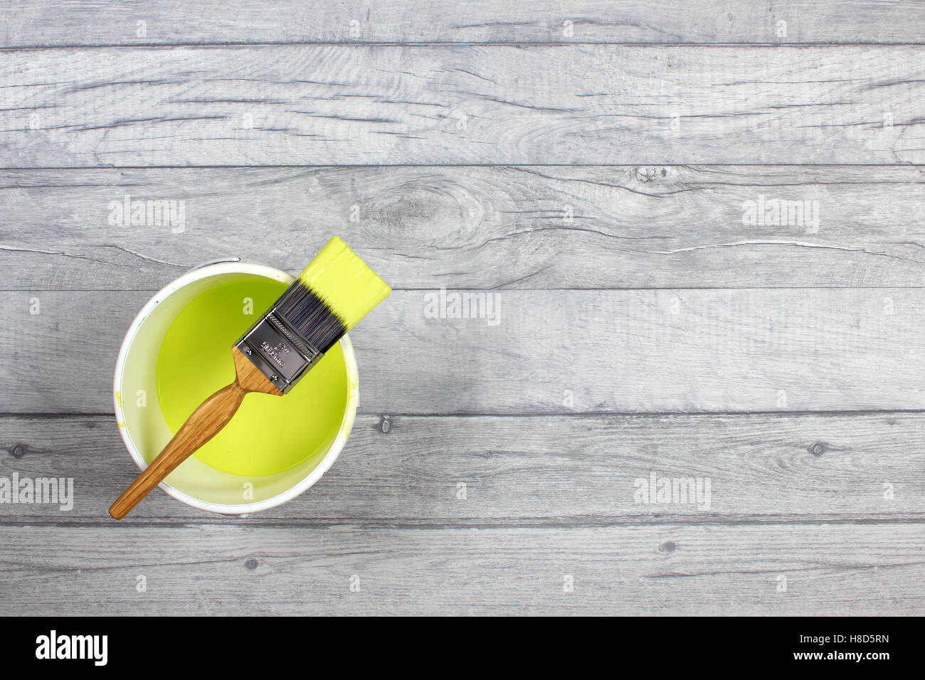 Loaded paintbrush placed across a white paint kettle filled with lime paint on a grey shabby style wood floor Stock Photo