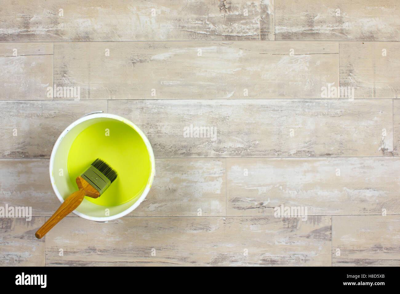 Paintbrush sitting in a white paint kettle filled with lime green paint on a shabby style wood floor Stock Photo