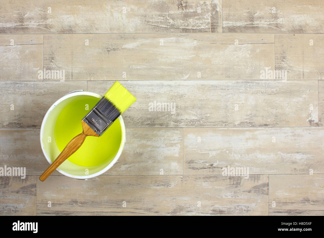 Loaded paintbrush placed across a white paint kettle filled with lime green paint on a shabby style wood floor Stock Photo