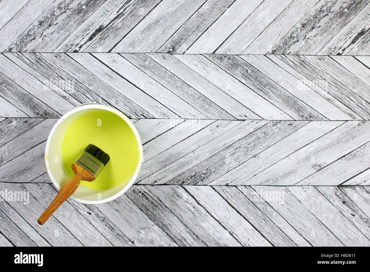 Paintbrush sitting in a white paint kettle filled with lime green paint on a grey and white herringbone style wood floor Stock Photo