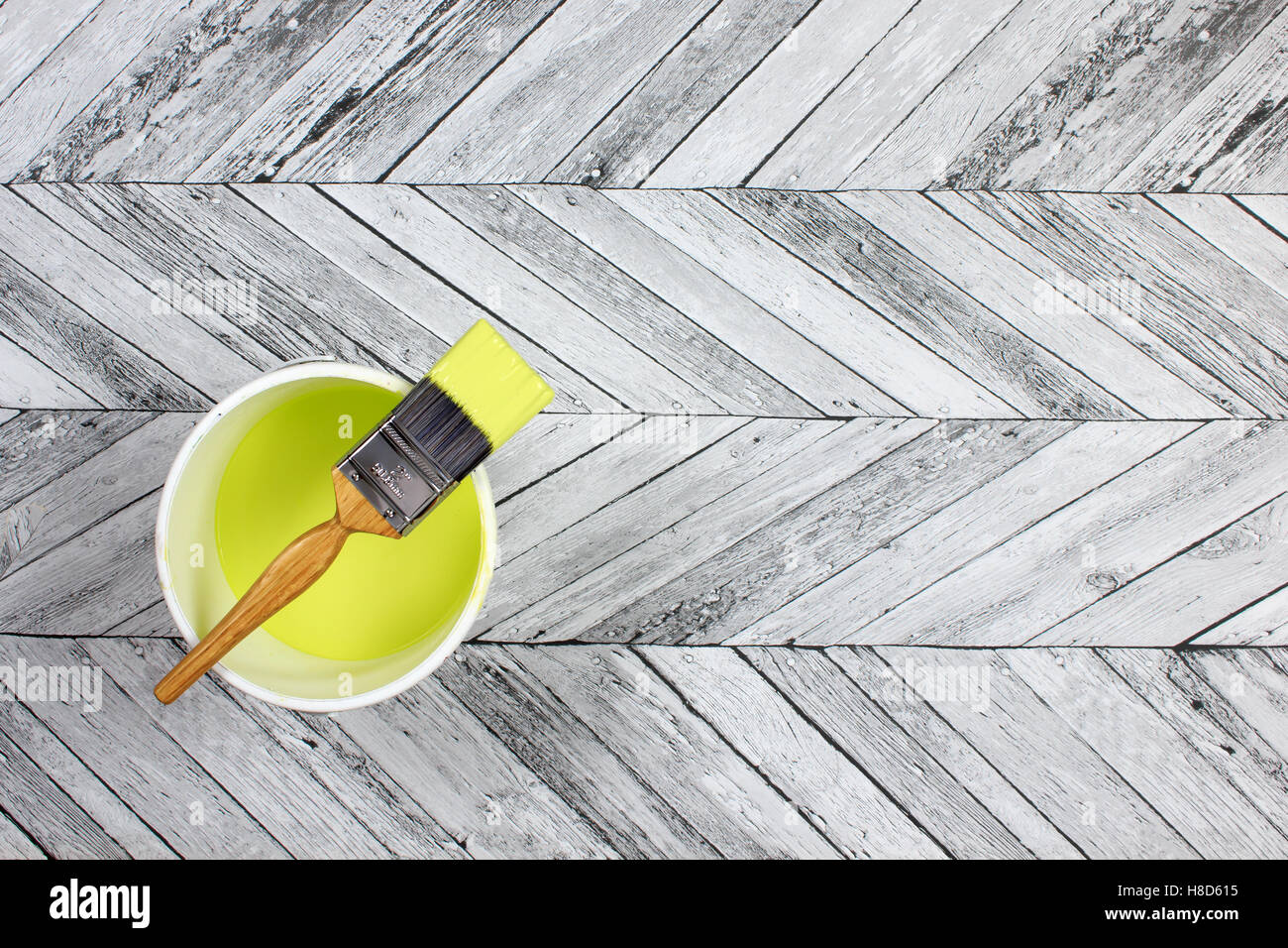 paintbrush placed across a white paint kettle filled with lime green paint on a grey and white herringbone style wood floor Stock Photo