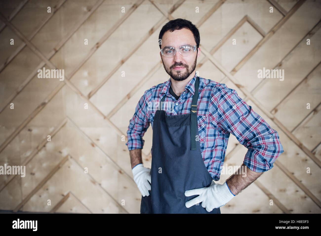 Young male carpenter wearing gloves and glasses with hands on hips Stock Photo