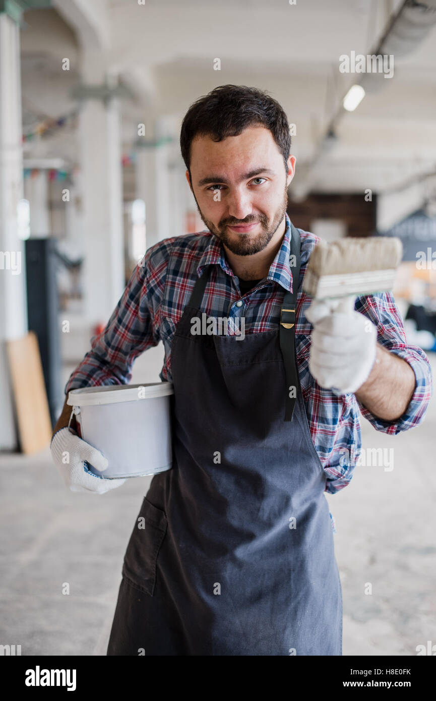 Happy young painter holding paint brush and showing it to camera Stock