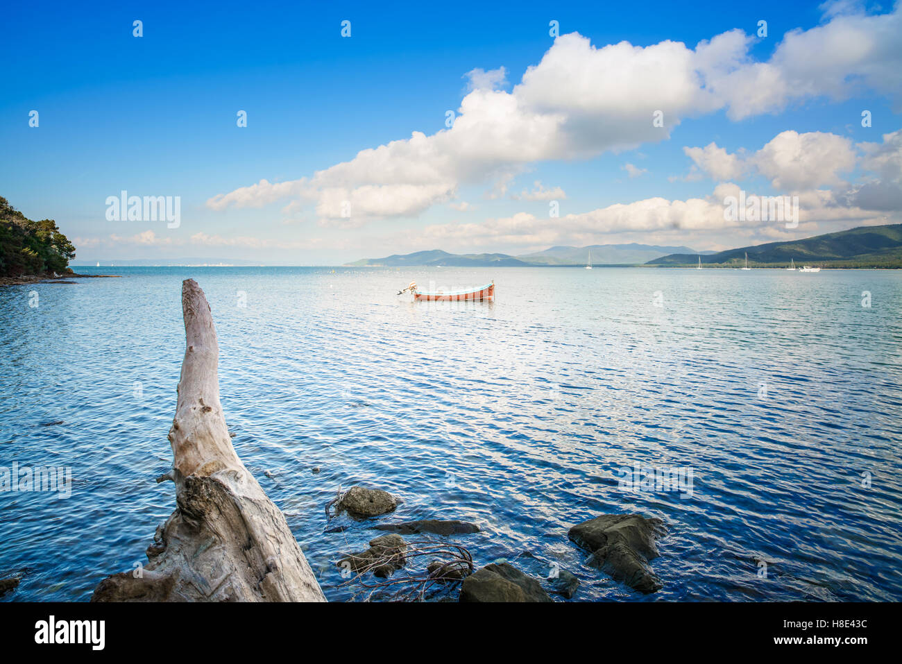 Small wooden boat and tree trunk in a sea bay on sunset. Punta Ala, Tuscany, Italy Stock Photo